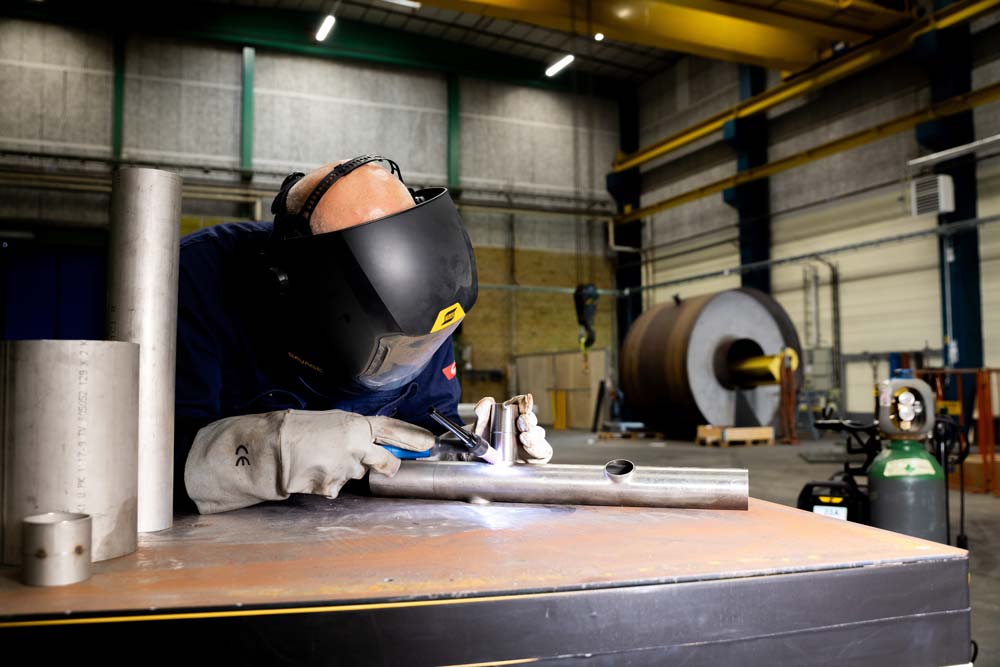  Ein Mann mit einem ESAB-Schweißhelm schweißt mit einem TBI-WIG-Brenner ein Metallobjekt, konzentriert auf seine Aufgabe.