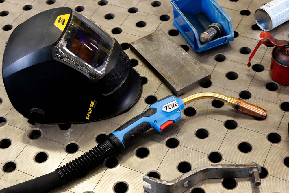 TBi-Mig-Brenner mit ESAB-Helm und anderem Zubehör auf einem Metallschweißtisch.