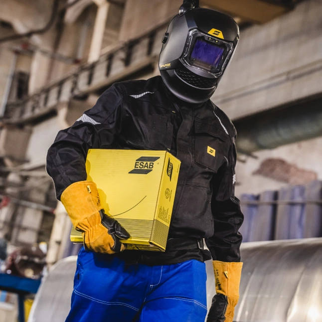 Welder holding ESAB welding consumables packaging in an industrial workshop