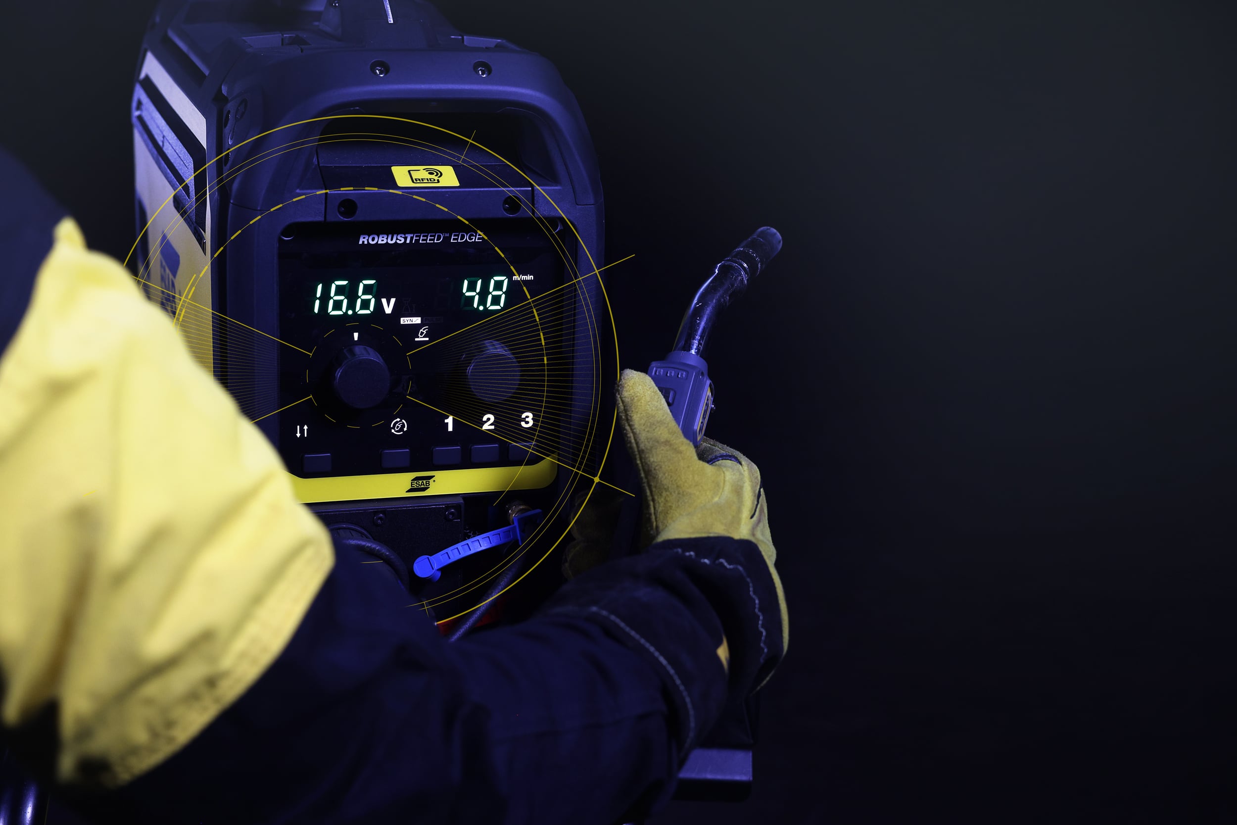 Welder holding an ESAB RobustFeed Edge machine in a dark room with panel on. 