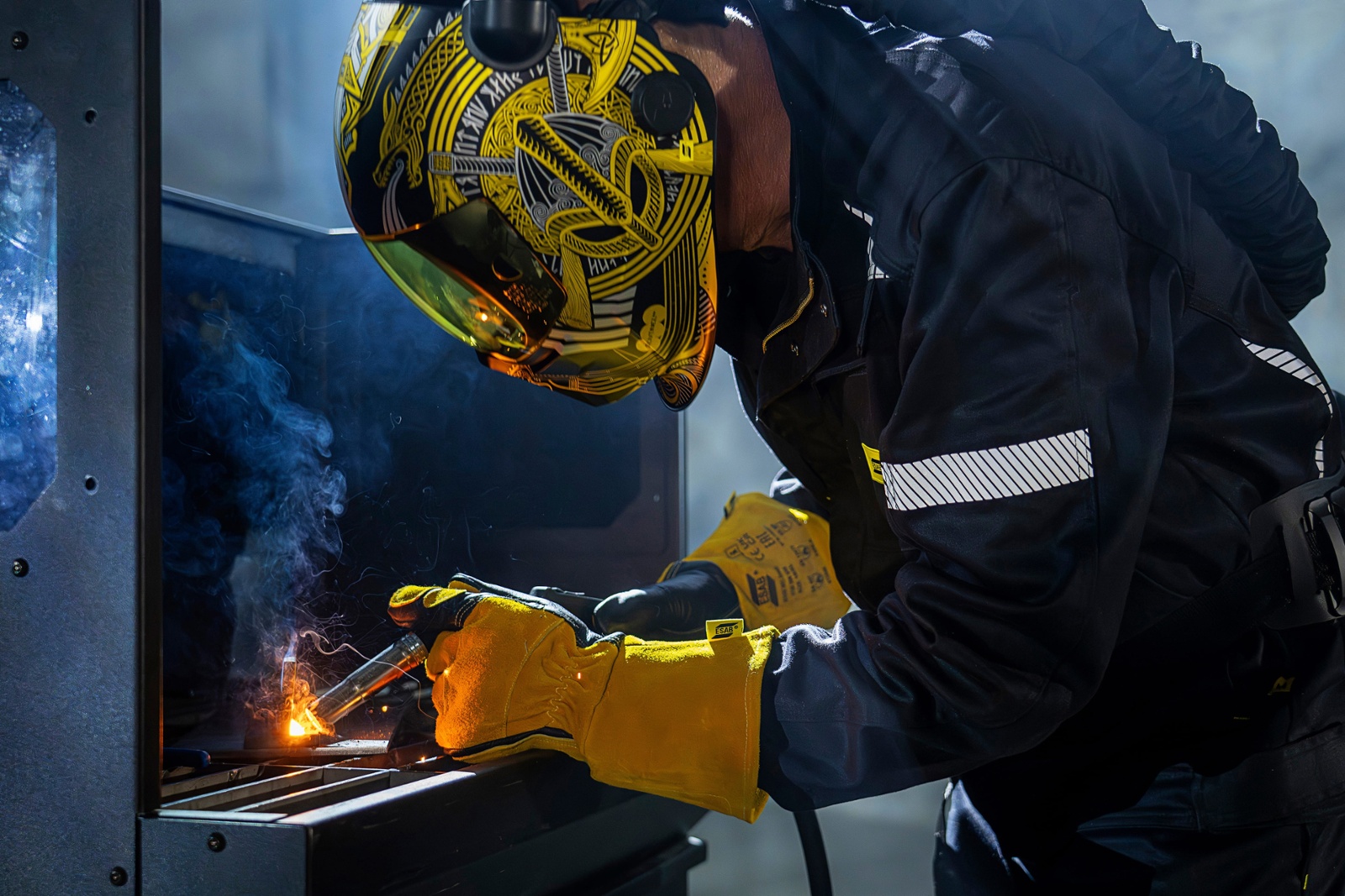 A welder in a welding suit uses a Rustler MIG PRO compact 350C Synergic welder to join a piece of metal.