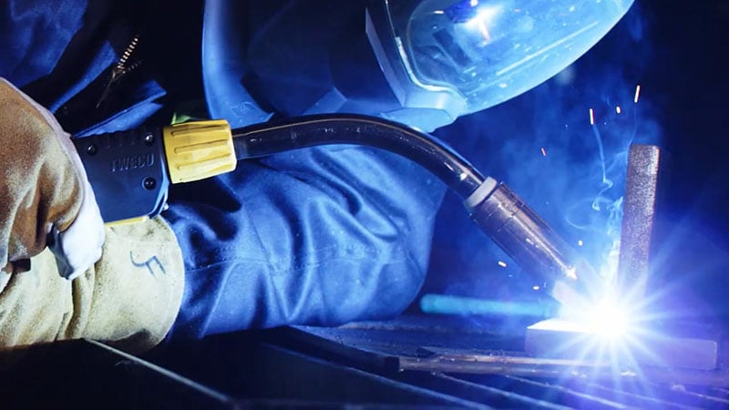 Close-up of MIG welding with Tweco gun producing arc and sparks during metal fabrication.