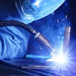Close-up of MIG welding with Tweco gun producing arc and sparks during metal fabrication.
