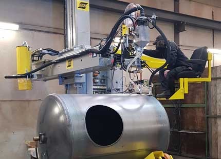 Un saldatore in una fabbrica sta lavorando su un serbatoio. Il dispositivo è dotato di supporto a rulli autoallineante del sistema CaB ESAB.